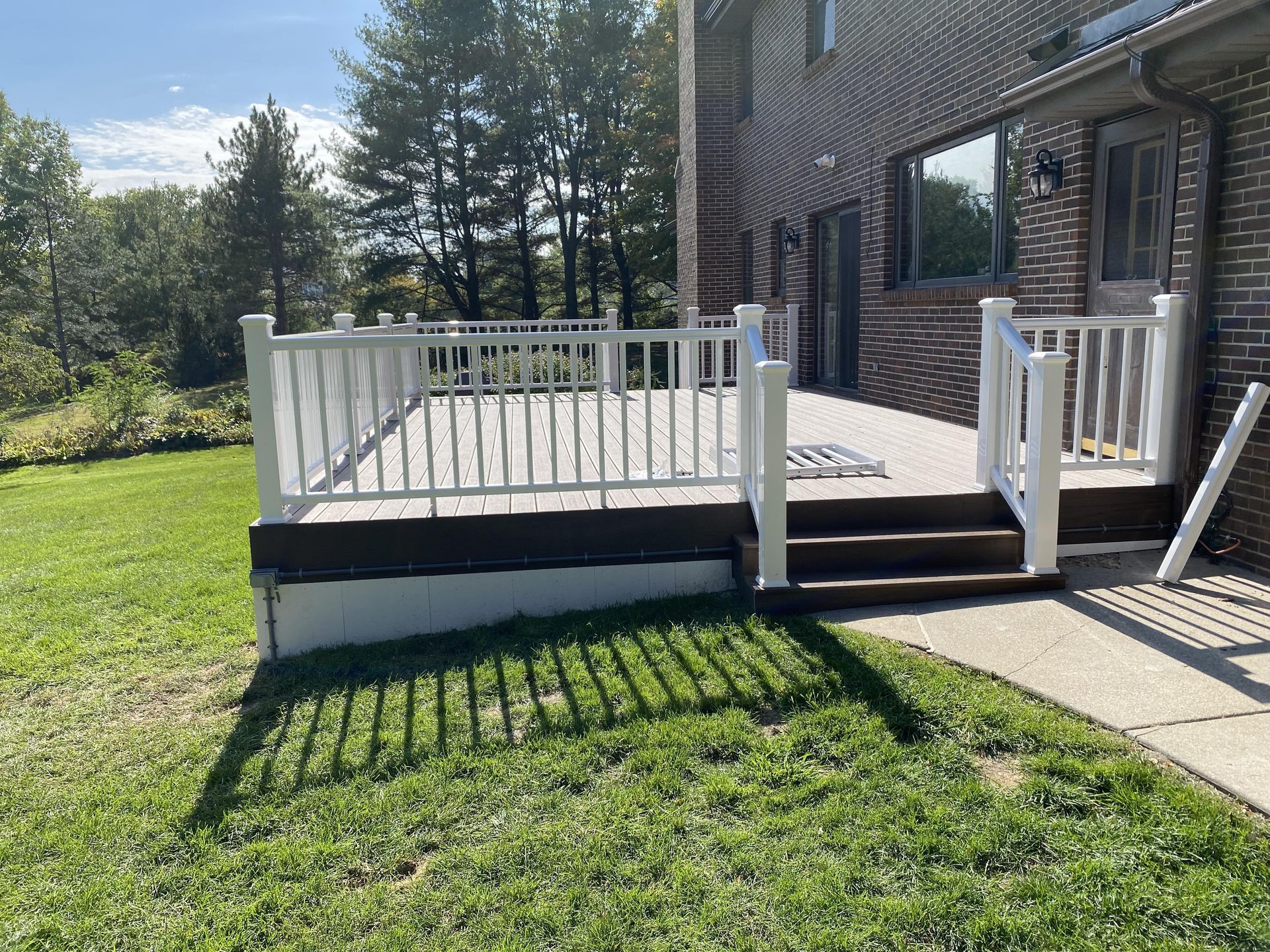 A large deck with stairs and a white railing in front of a brick house.