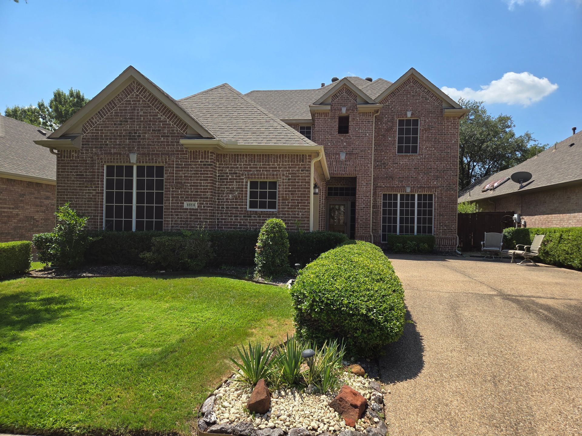 Brick suburban house with manicured lawn, driveway, and clear blue sky
