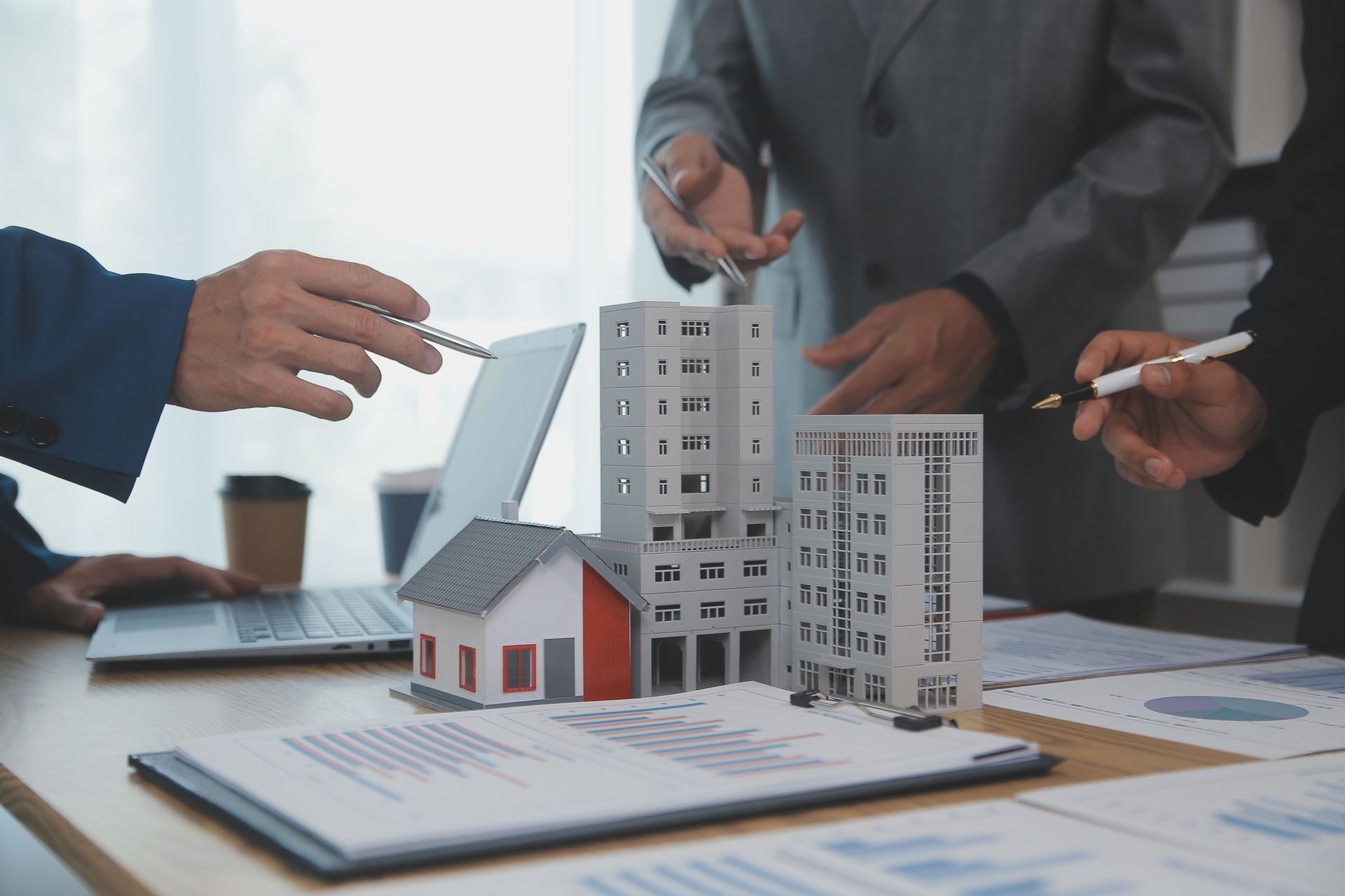 Hands discussing a scale model of buildings over architectural plans on a desk