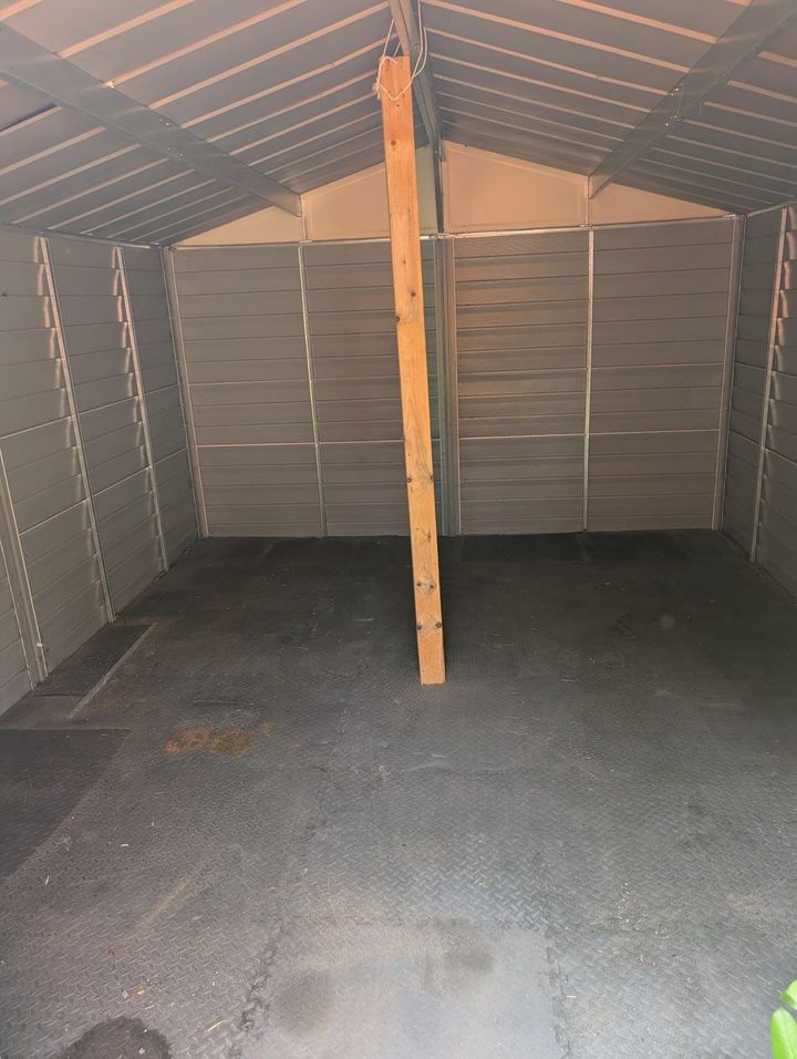 Interior view of a gray shed with a single vertical wooden support beam in the center and a dark floor.