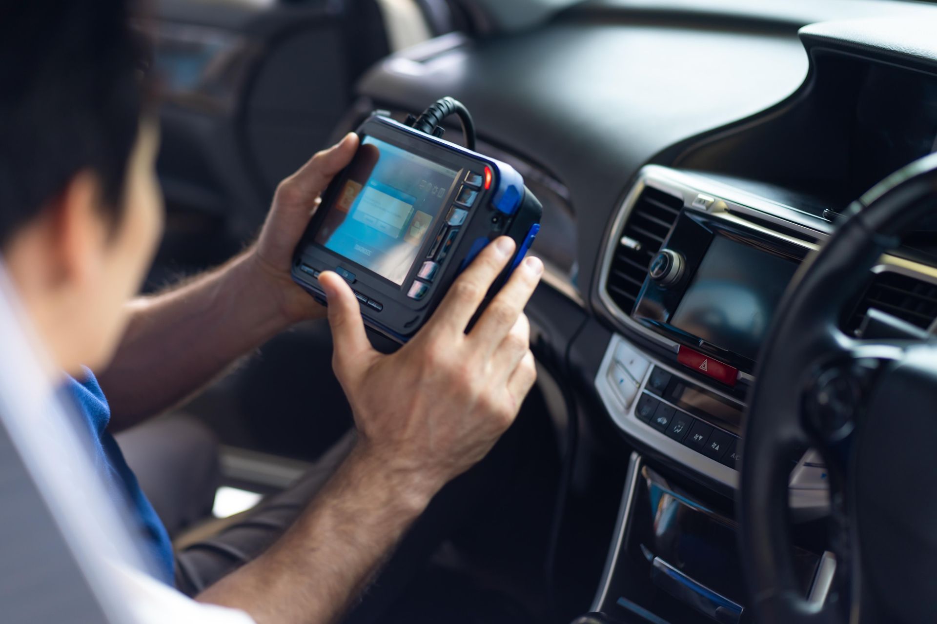 Person using a diagnostic tool inside a car to check engine issues.