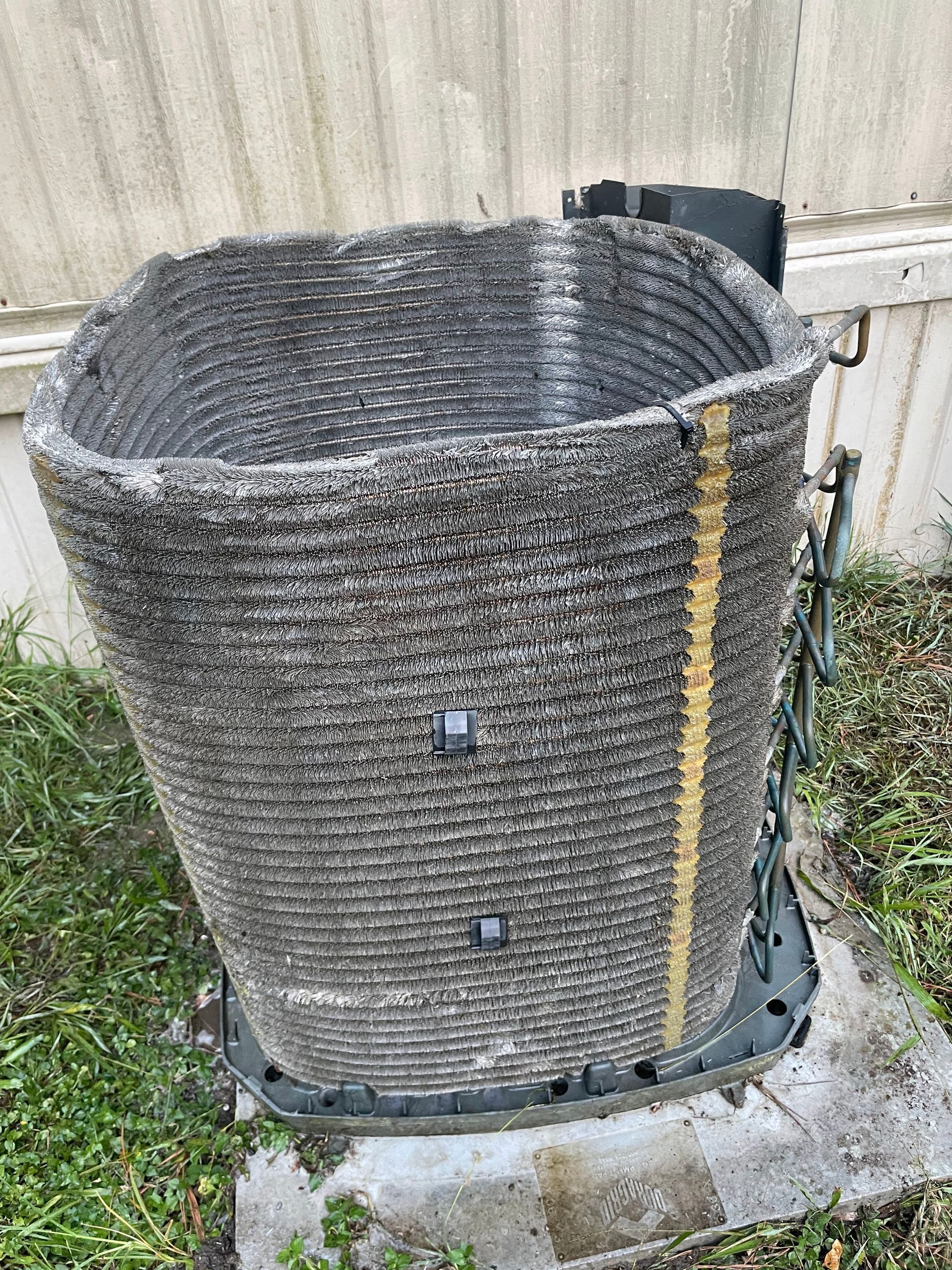 Outdoor air conditioning unit with heavily soiled coils, sitting on concrete base near grass.