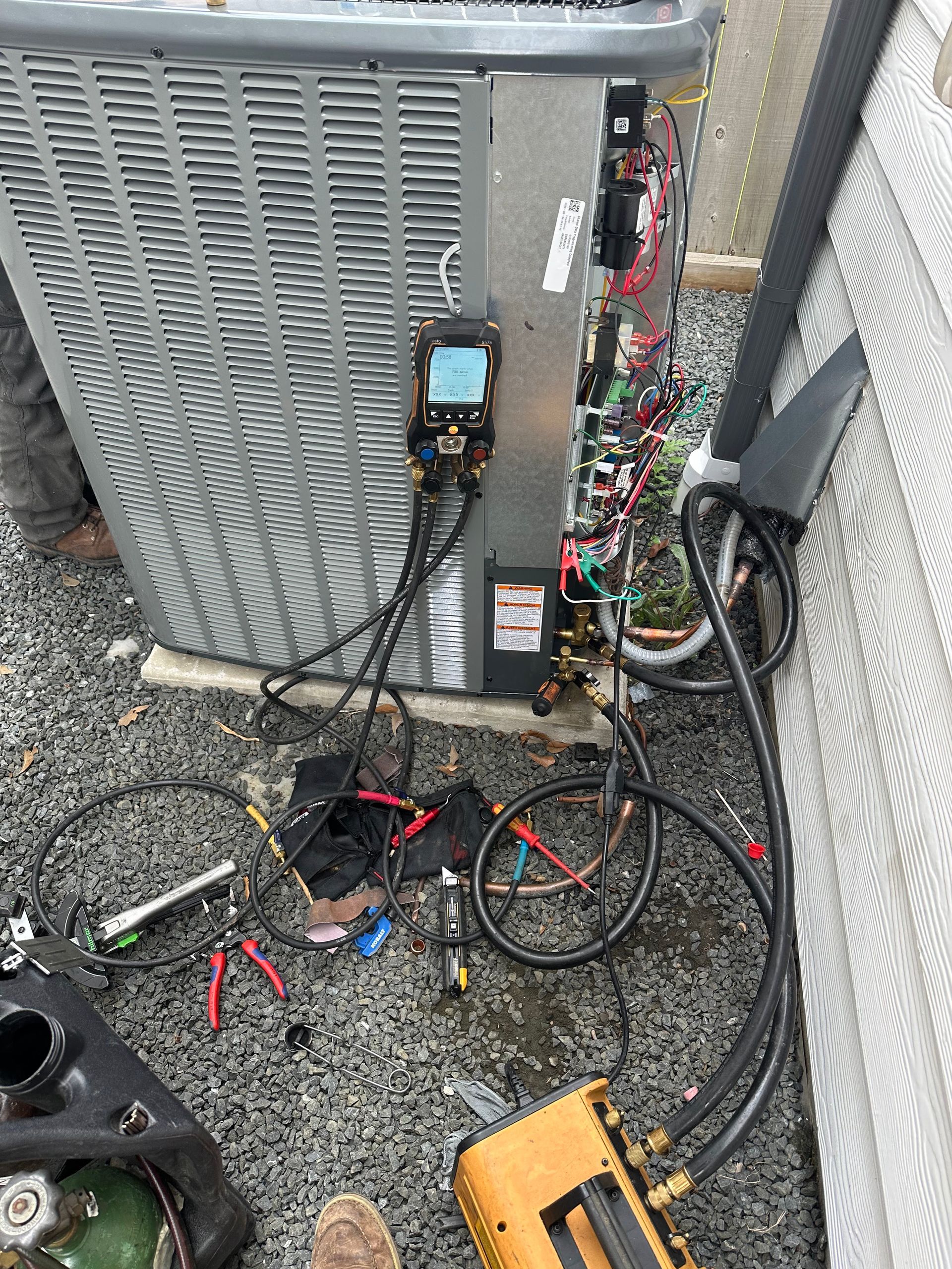 HVAC technician working on an outdoor air conditioning unit, using gauges and tools.