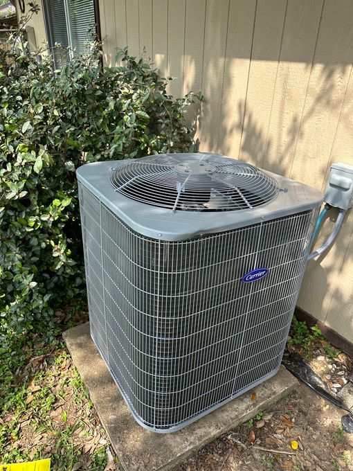 Air conditioning unit outside a building, surrounded by greenery.