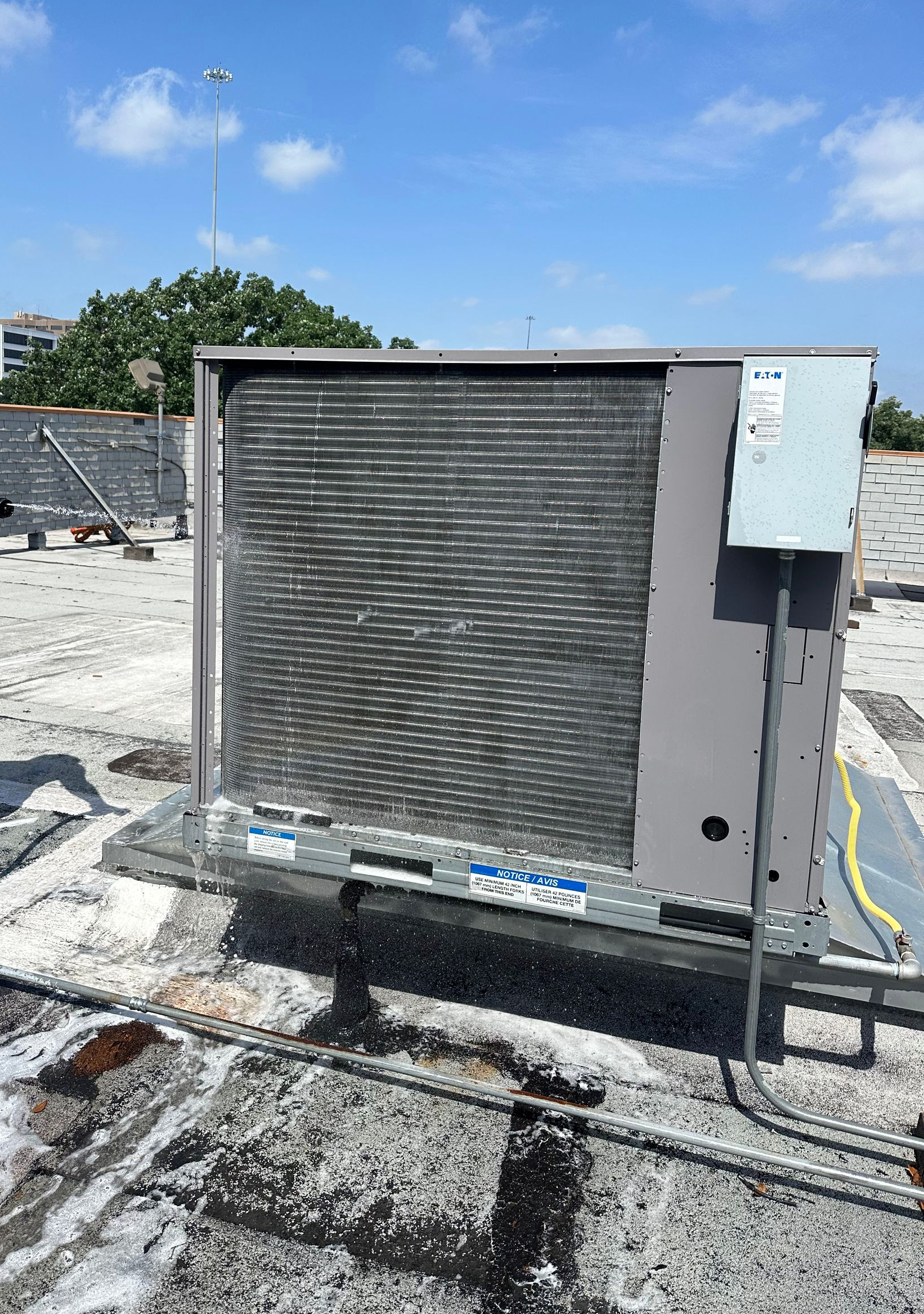 Rooftop air conditioning unit with silver coils, gray cabinet, and electrical box, against a blue sky.