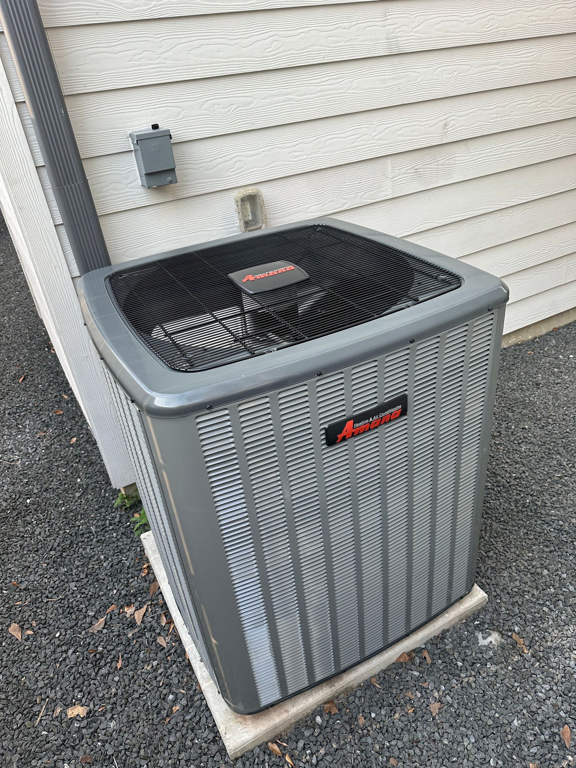 Outdoor air conditioning unit, gray metal, near a house with gray siding and gravel.