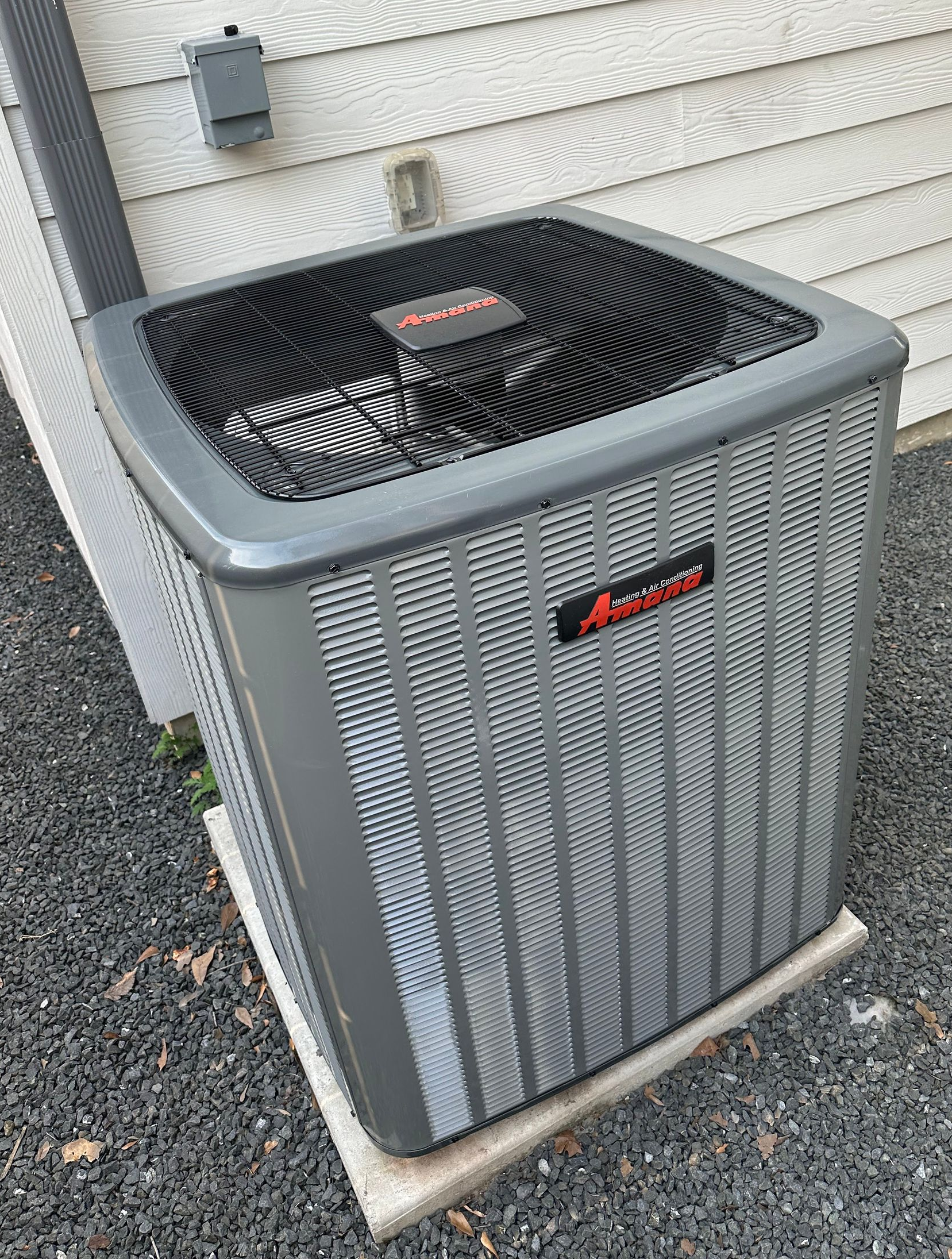 Gray air conditioning unit outside a building with gray siding and gravel.