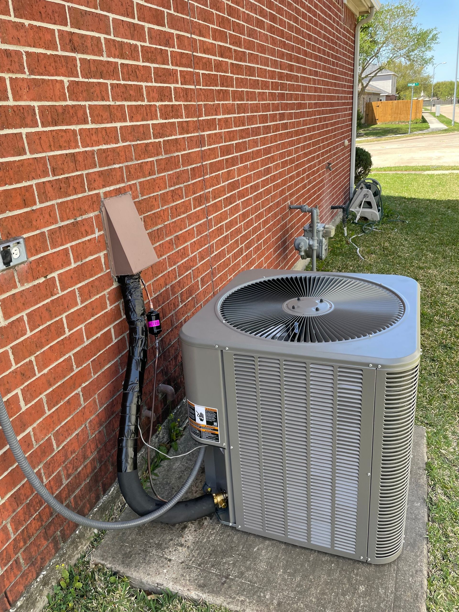 Air conditioning unit next to a brick wall with connected pipes and electrical components.