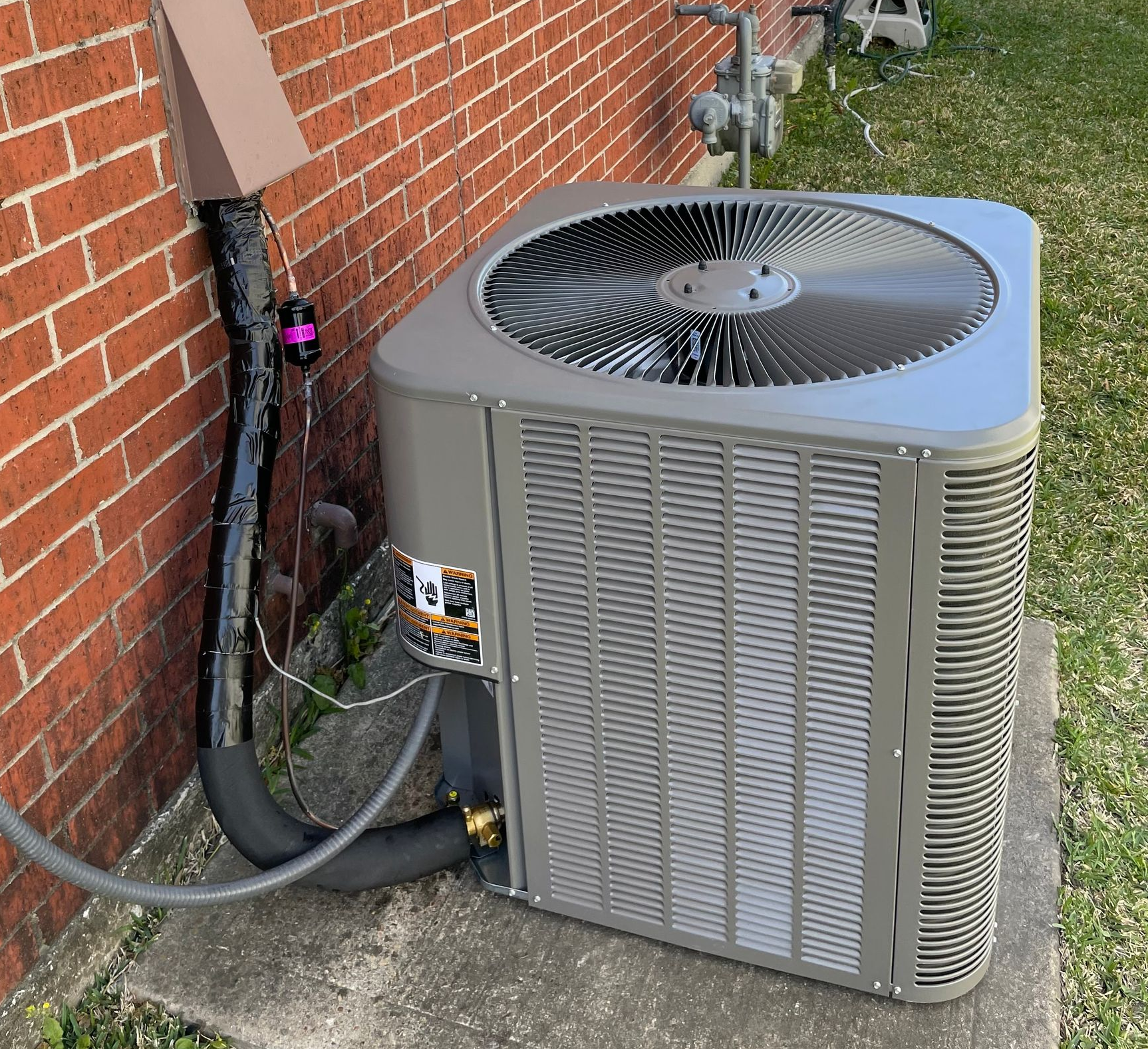Gray air conditioning unit next to a brick building.