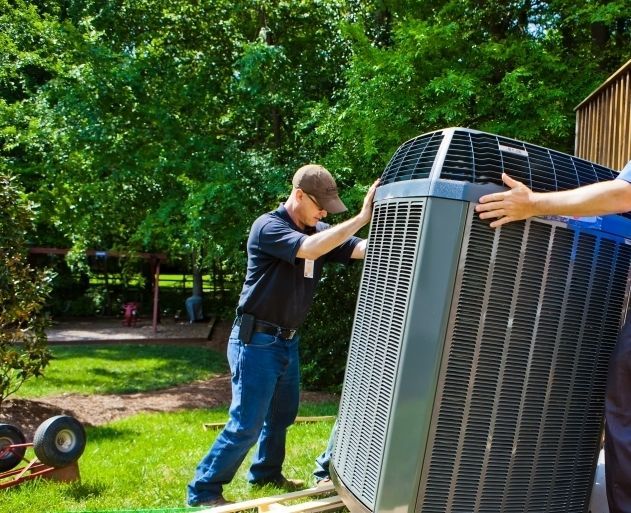 Two men installing an outdoor air conditioner unit in a yard.