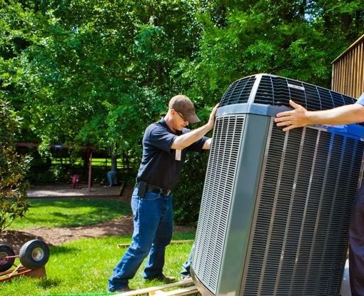 Two men installing an outdoor air conditioner unit in a yard.