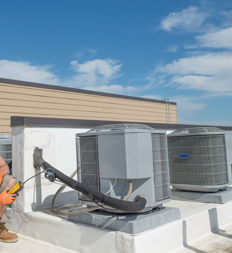 HVAC technician on a rooftop inspects air conditioning units under a blue sky.