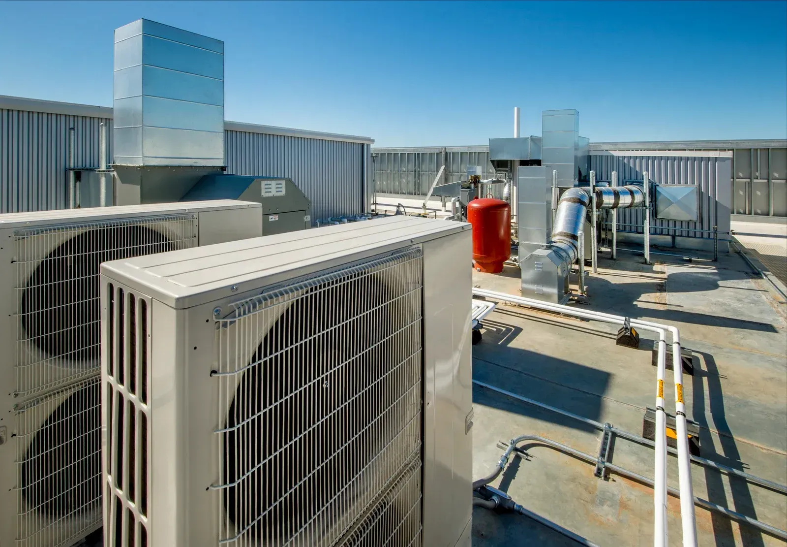 HVAC units and ductwork on a flat rooftop against a clear blue sky.