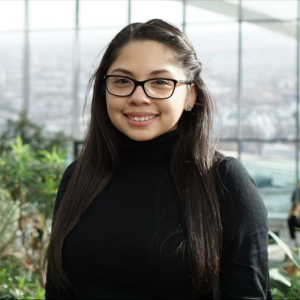 A woman wearing glasses and a black turtleneck smiles for the camera