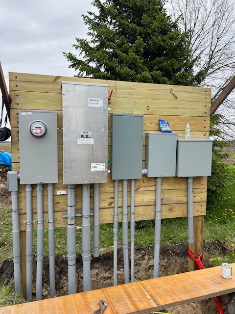 Electrical utility panels and conduit mounted on a wooden fence outdoors.