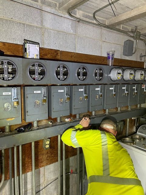 Electrician working on gray electrical panels in a basement utility room
