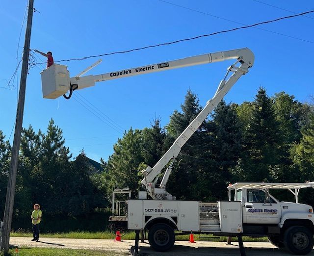 Utility bucket truck extended beside roadside trees under a clear blue sky