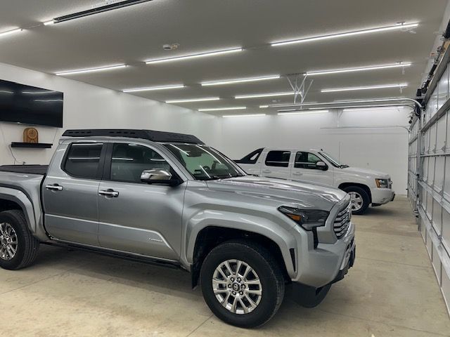 Two pickup trucks parked inside a bright garage, with a silver truck in front