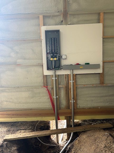 Electrical panel mounted on unfinished wall with conduit and pipes in a basement-like space