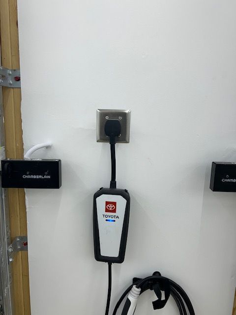 Wall outlet with a plugged-in black device and coiled cable mounted on a white door or panel