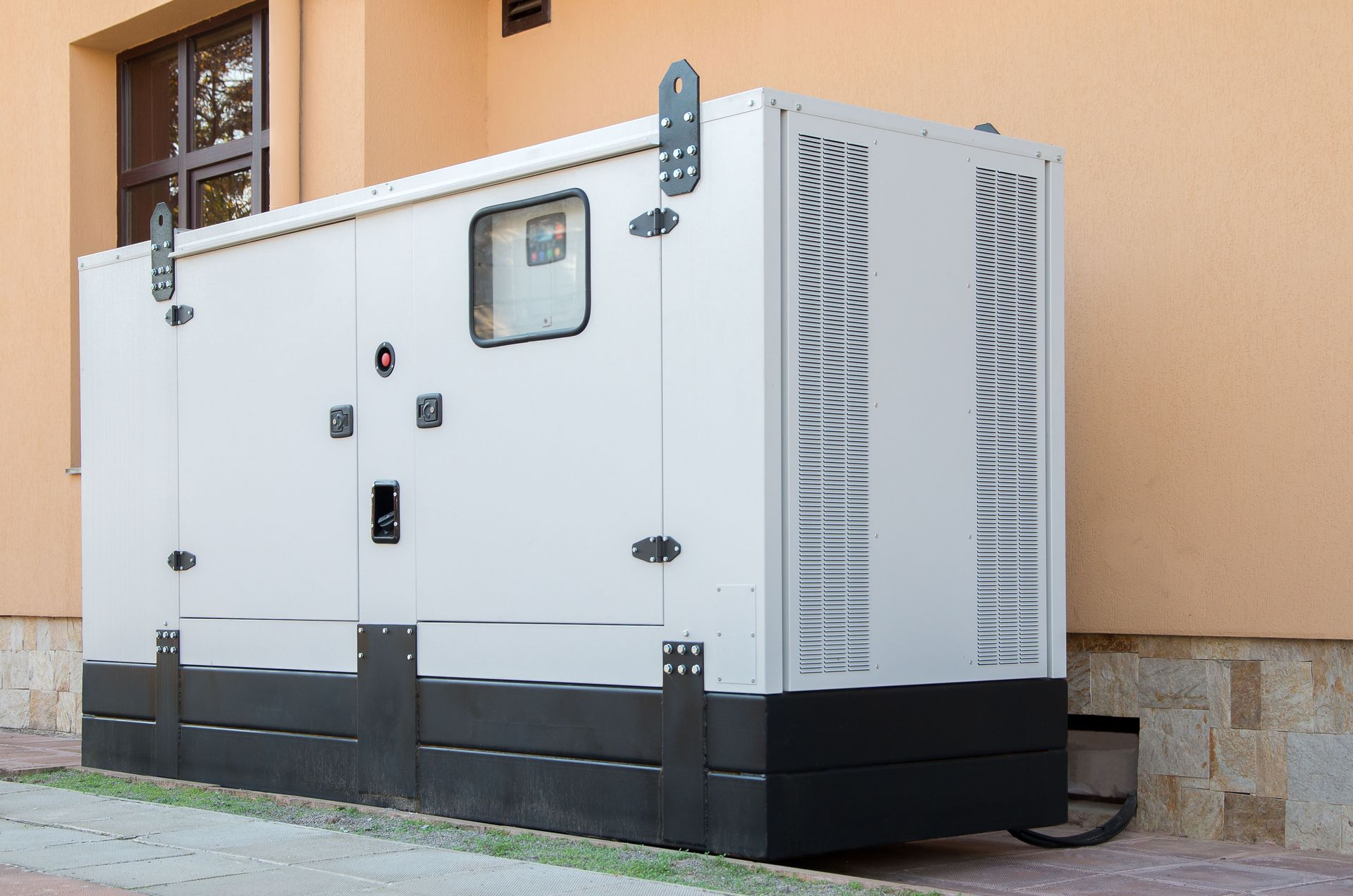 Large white industrial generator unit with vents, shown outdoors beside a building.