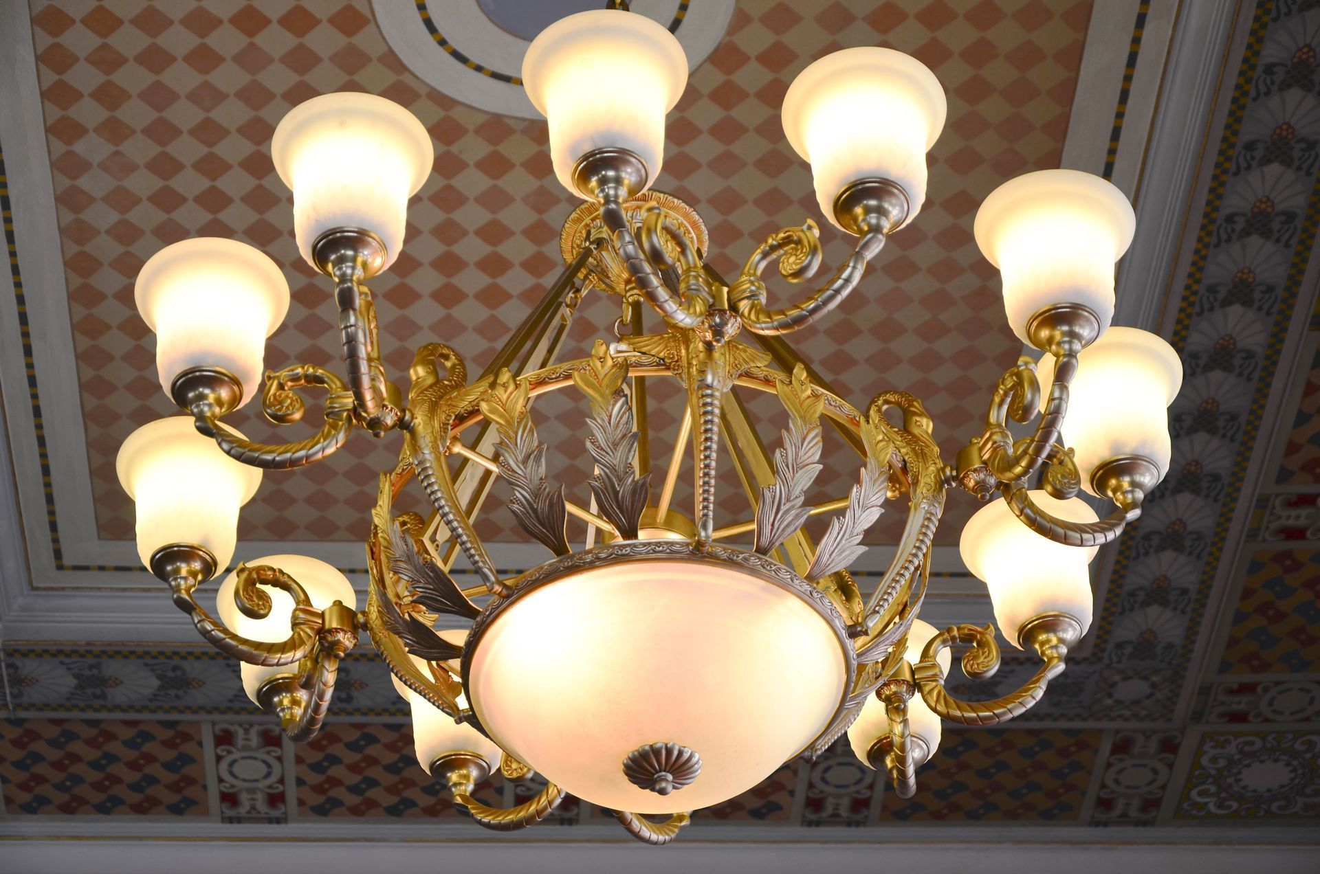Ornate gold chandelier with frosted glass shades hanging from a decorated ceiling