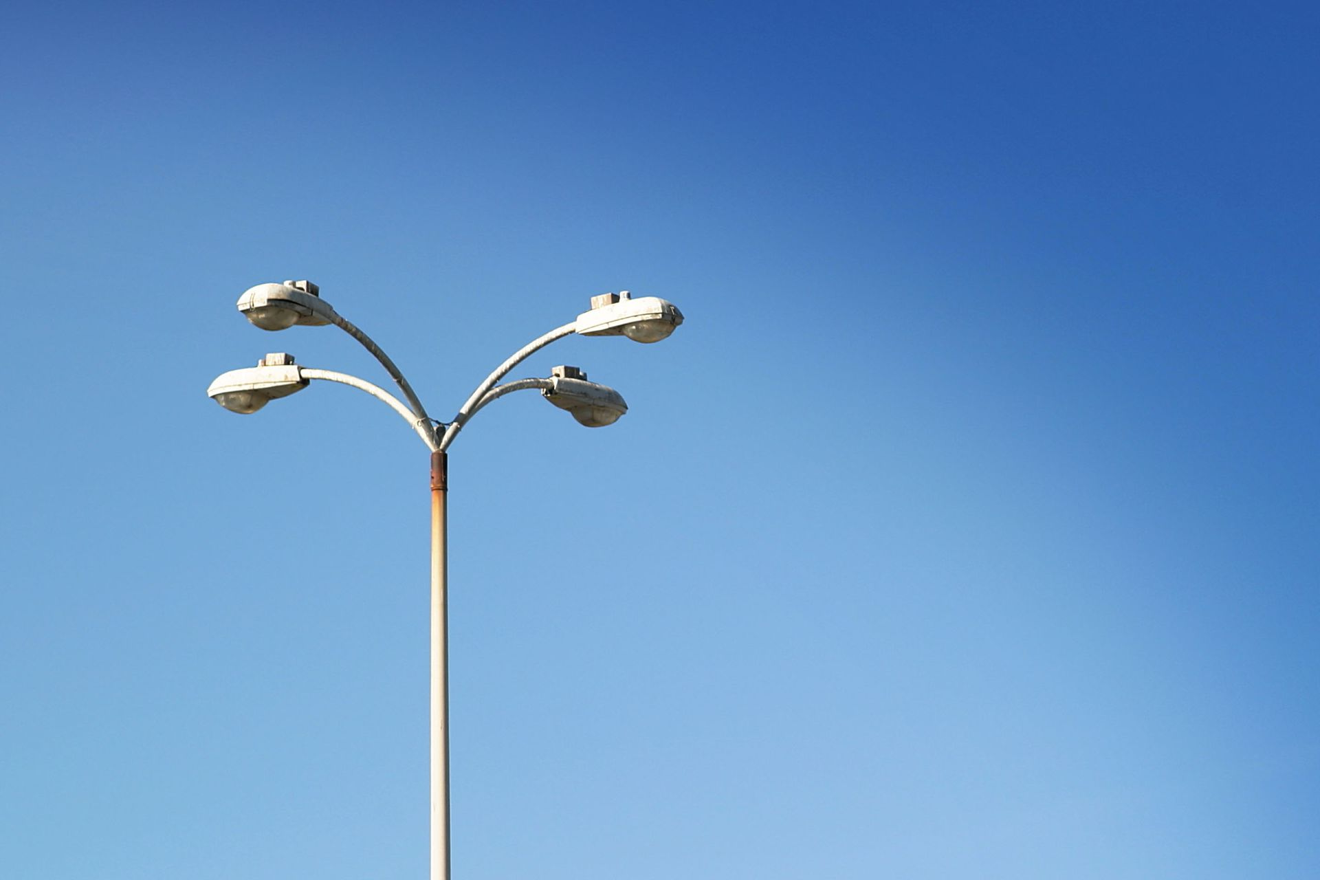 Tall streetlight with three lamps against a clear blue sky