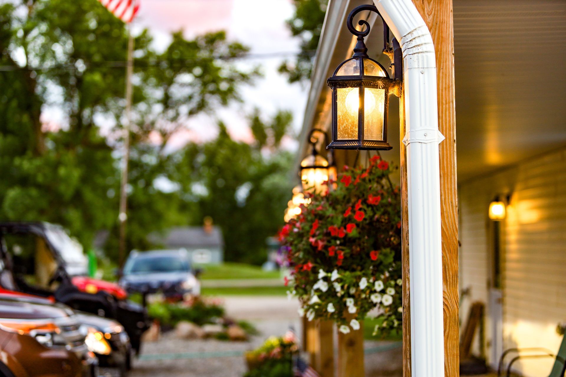 Flowering hanging baskets and lanterns line a porch outside a charming storefront at dusk.