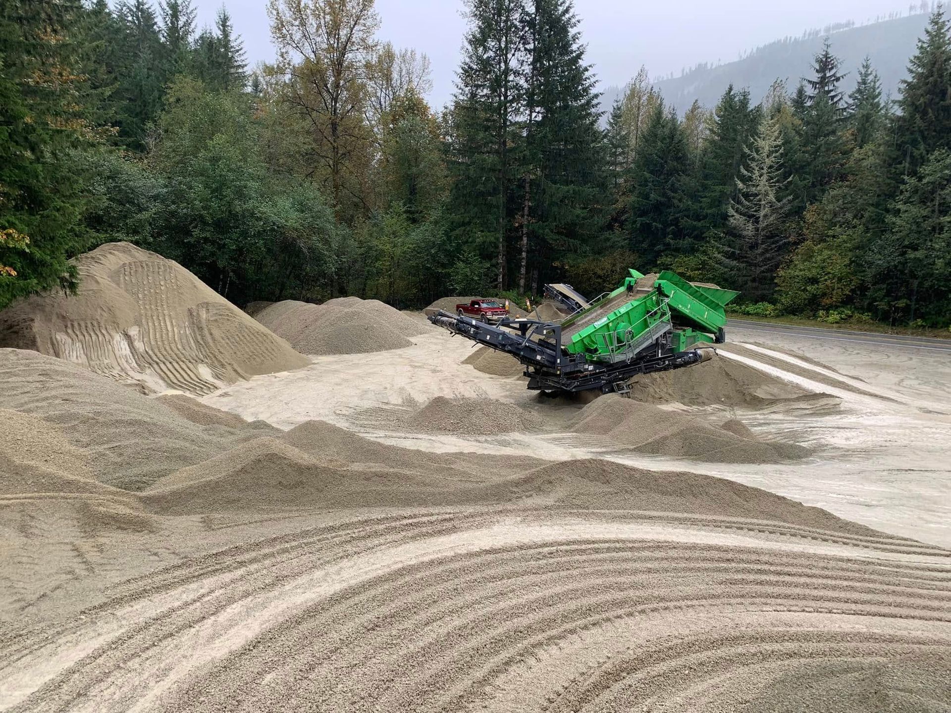 Green rock crusher sorting gravel in a forest clearing.