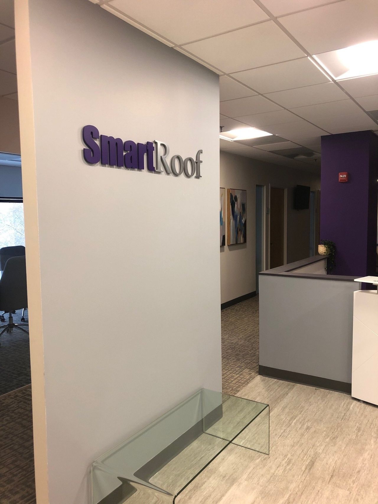 SmartRoof office lobby with purple logo, reception desk, and glass bench on light wood flooring