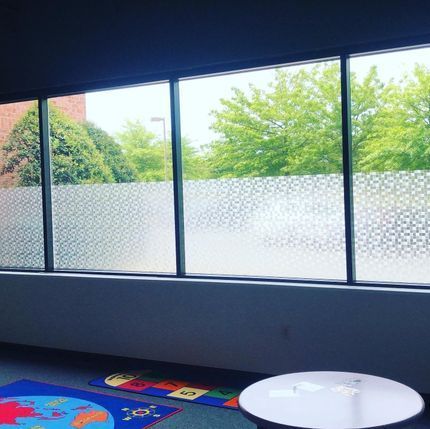 Large window with frosted lower panes, trees outside, and a colorful play rug with a white round table.