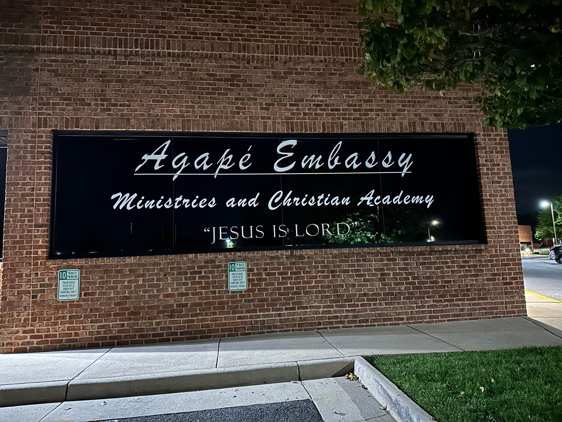 Sign for Agape Embassy Ministries and Outreach Academy on a brick wall at night