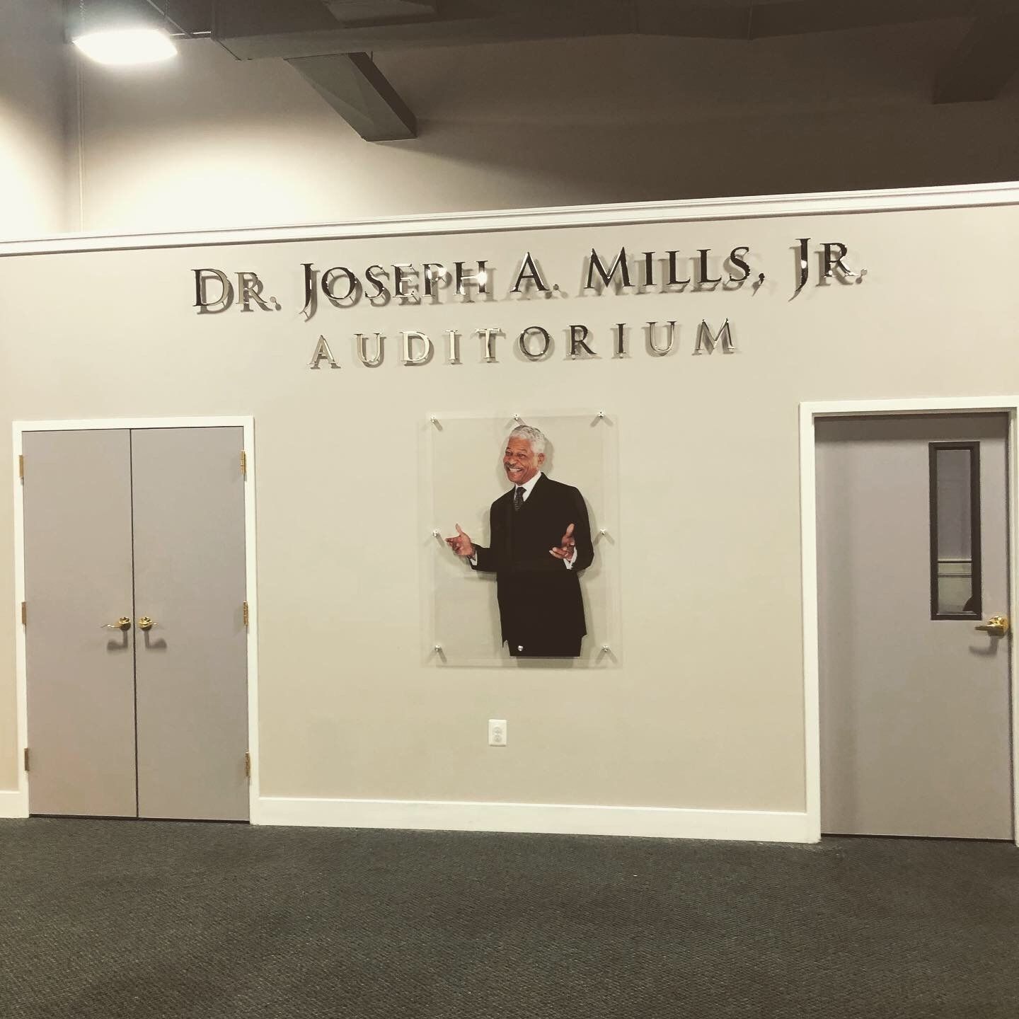 Auditorium wall labeled “Dr. Joseph A. Mills, Jr. Auditorium” with a portrait and two doors