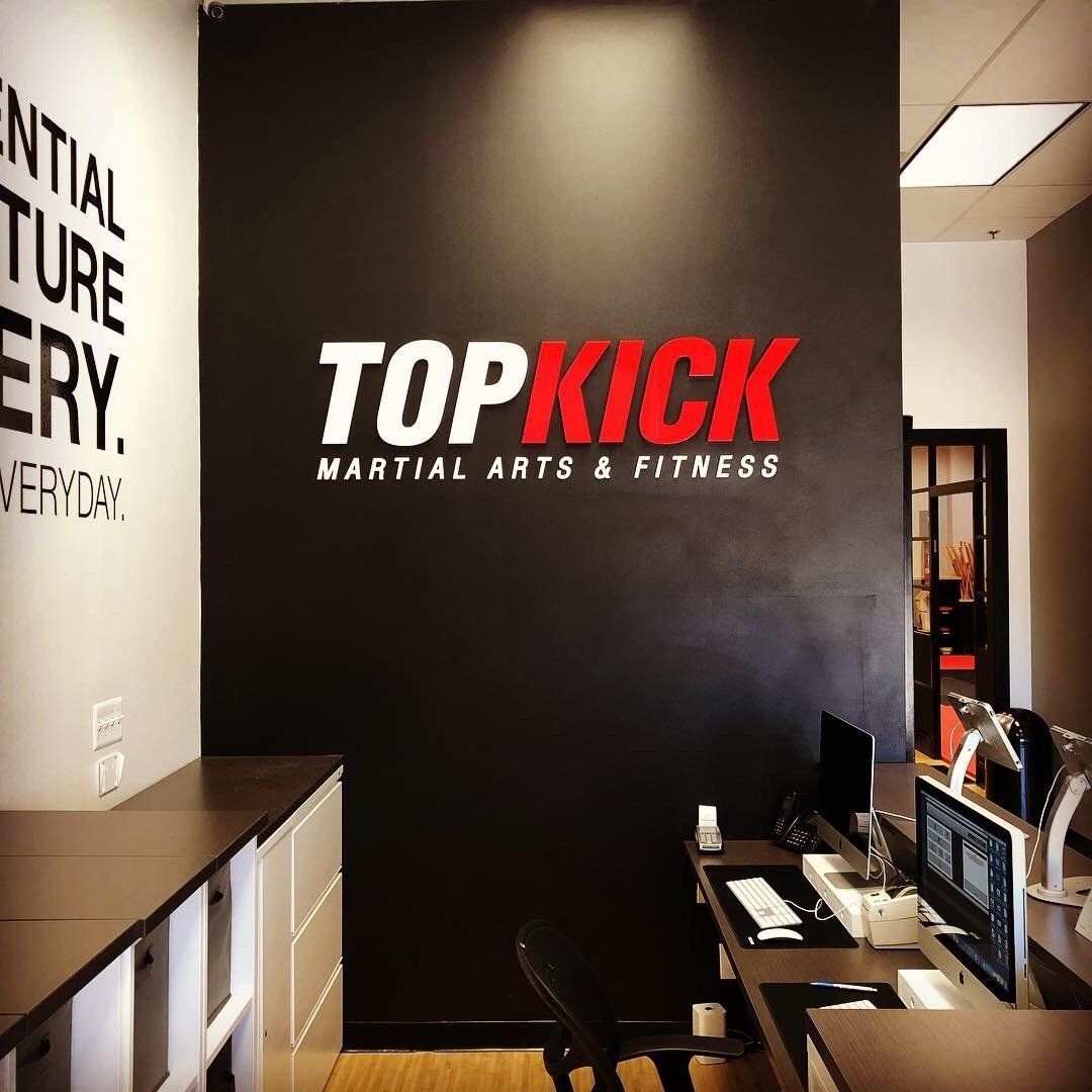 Top Kick Martial Arts & Fitness logo on a black wall in a gym reception area