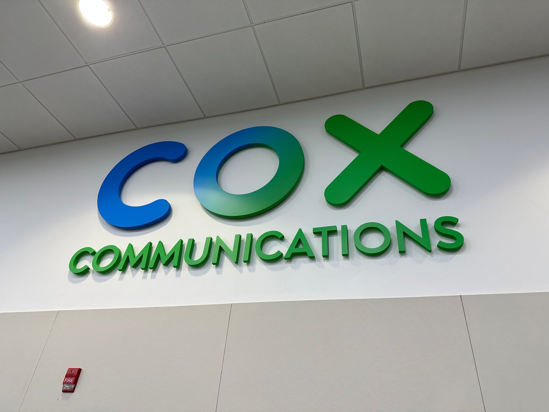Cox Communications logo in blue and green on a wall inside an office lobby