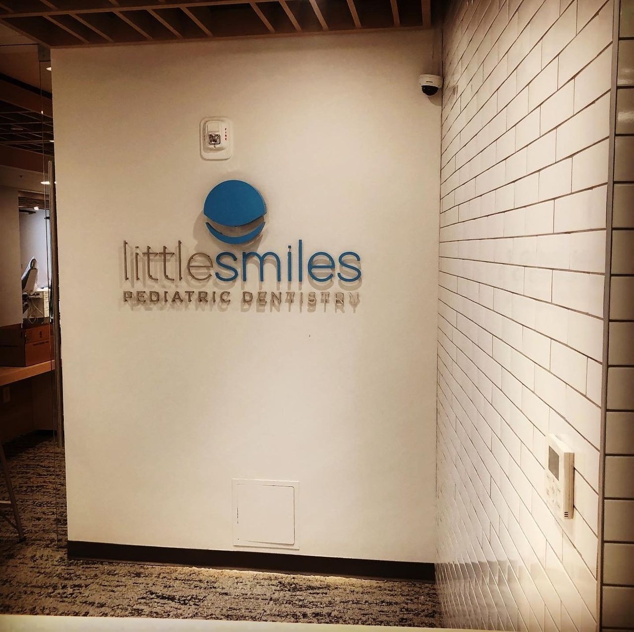 Clinic hallway with a wall sign reading “littlesmiles pediatric dentistry” in blue and gray.