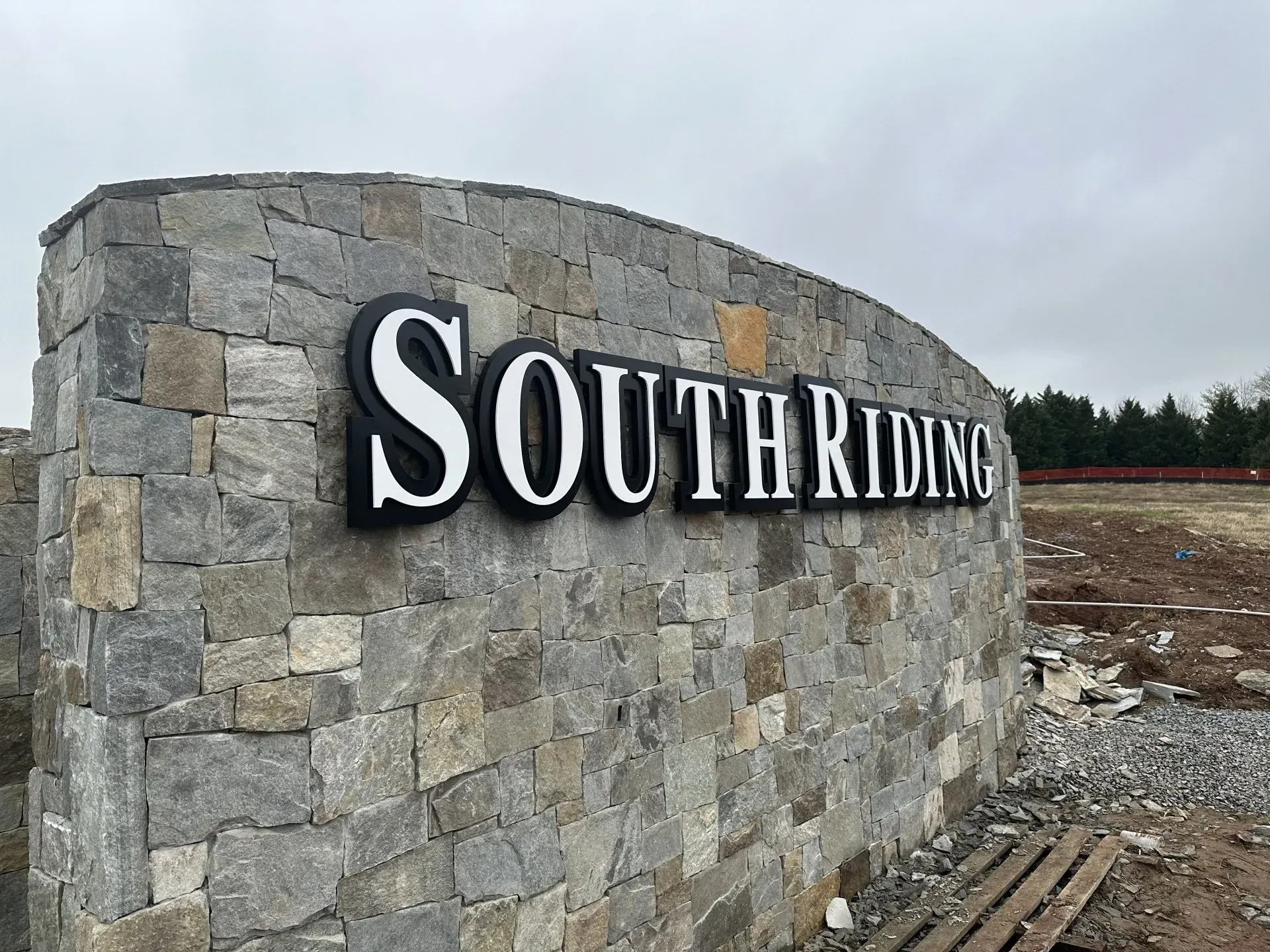 Stone wall entrance sign reading “South Riding” under a cloudy sky