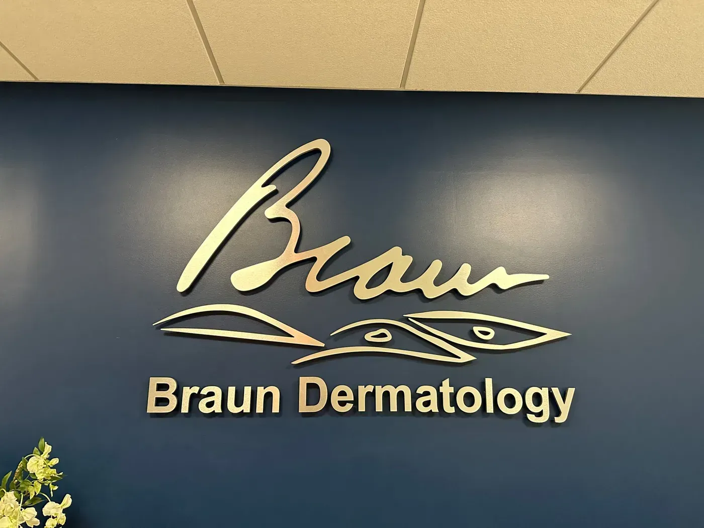 Braun Dermatology gold logo on dark blue wall with floral accents
