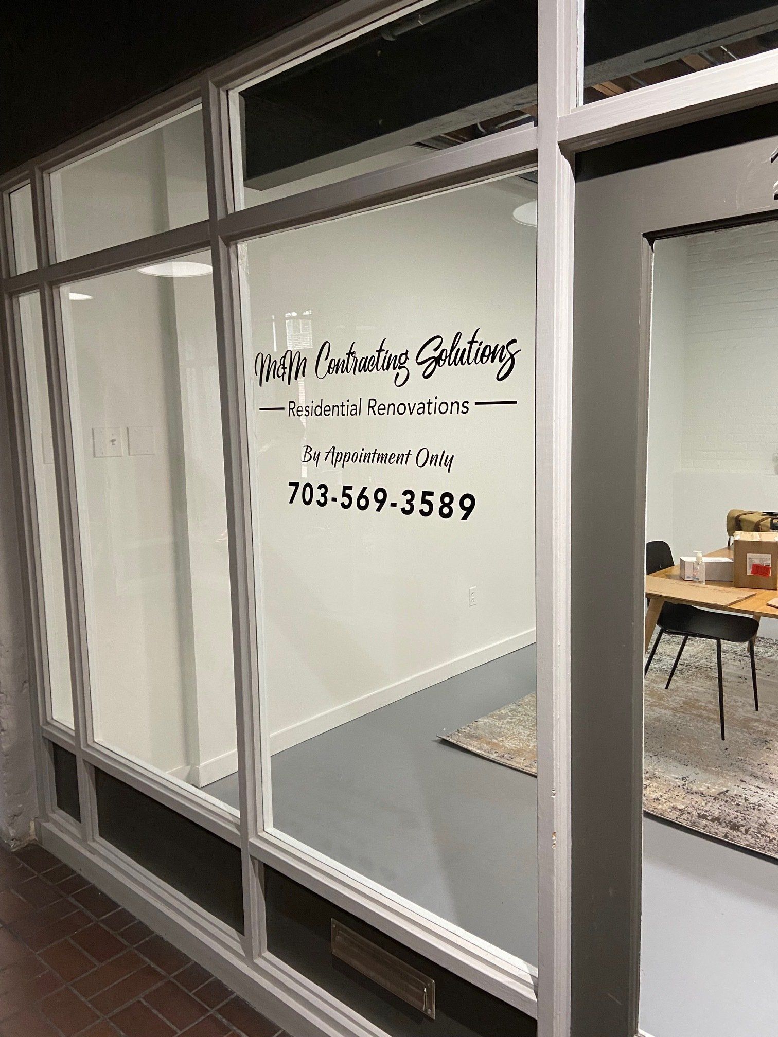 Storefront window with lettering and phone number, viewed from outside.