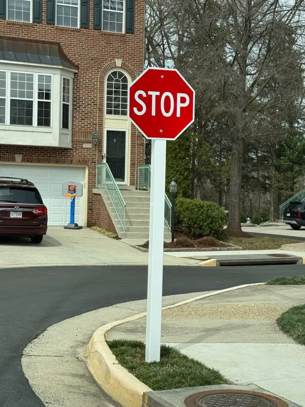 Red stop sign on a white pole at a suburban street corner near houses and parked cars.