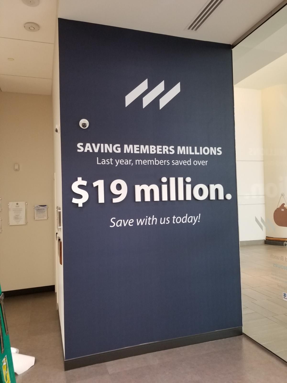 Blue wall sign advertising “$19 million” savings with white text and logo in an office hallway