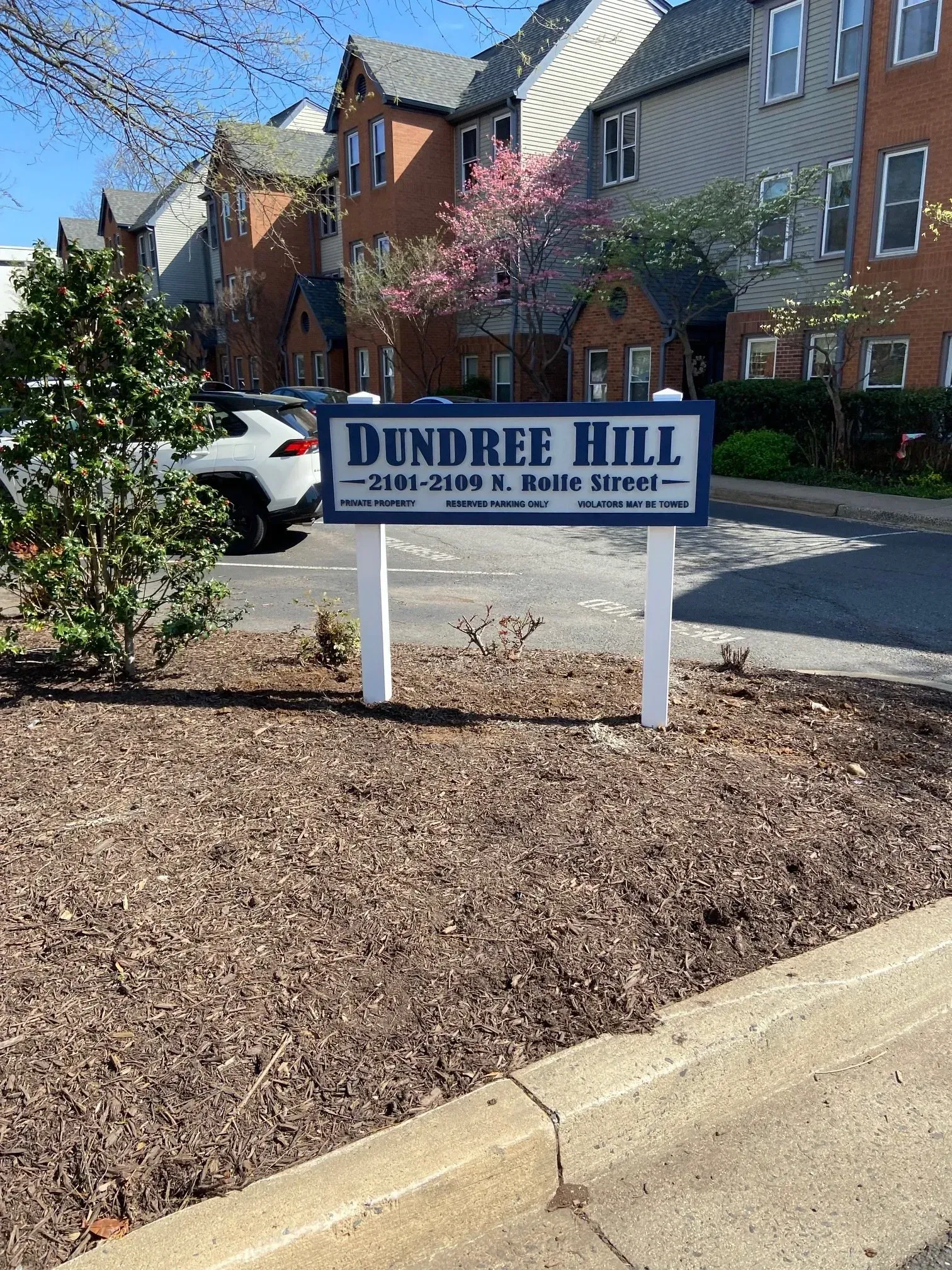 Dundee Hill apartment sign in front of brick buildings and parked cars on a sunny day