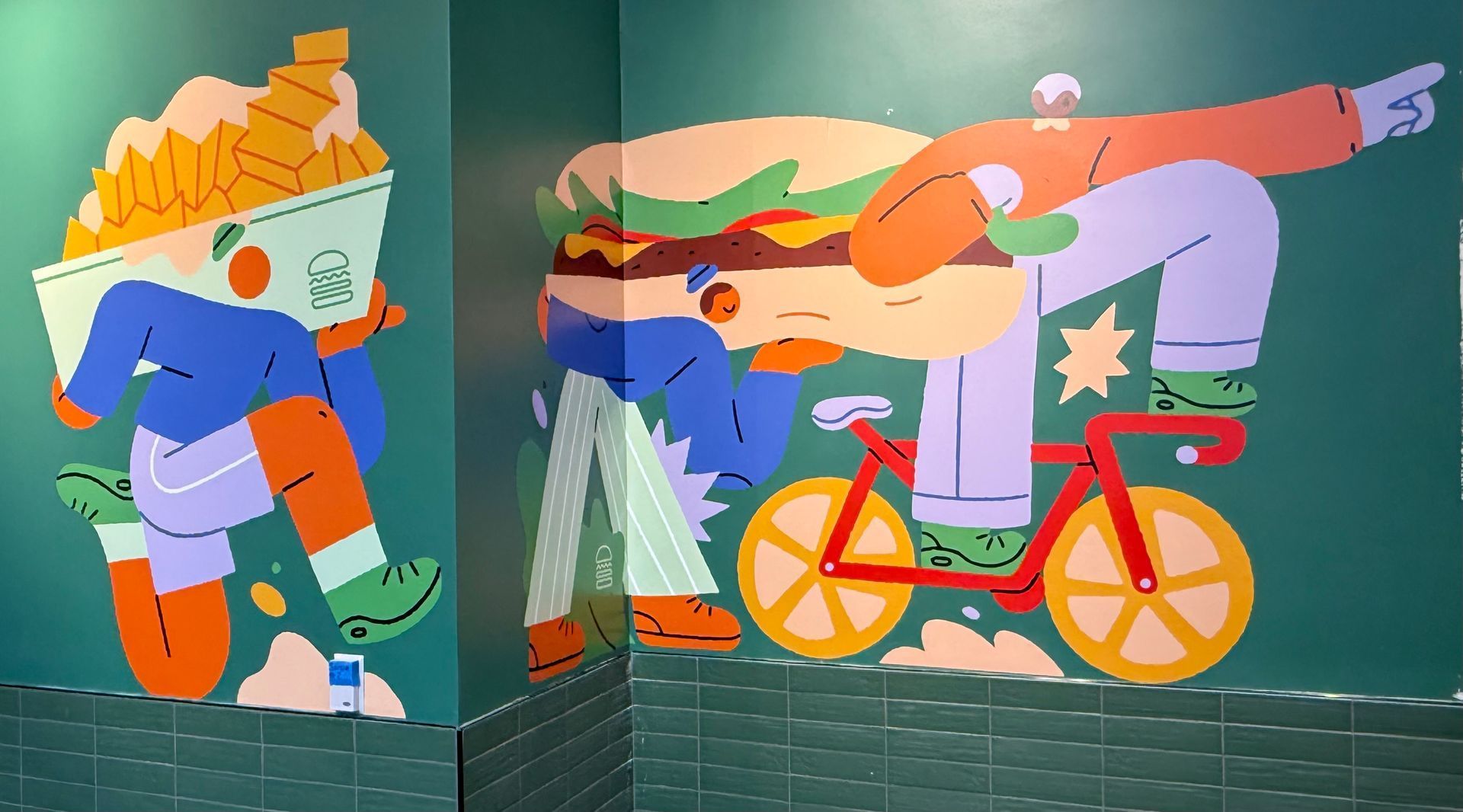 Child riding a pink bicycle through a colorful mural of food and city scenes