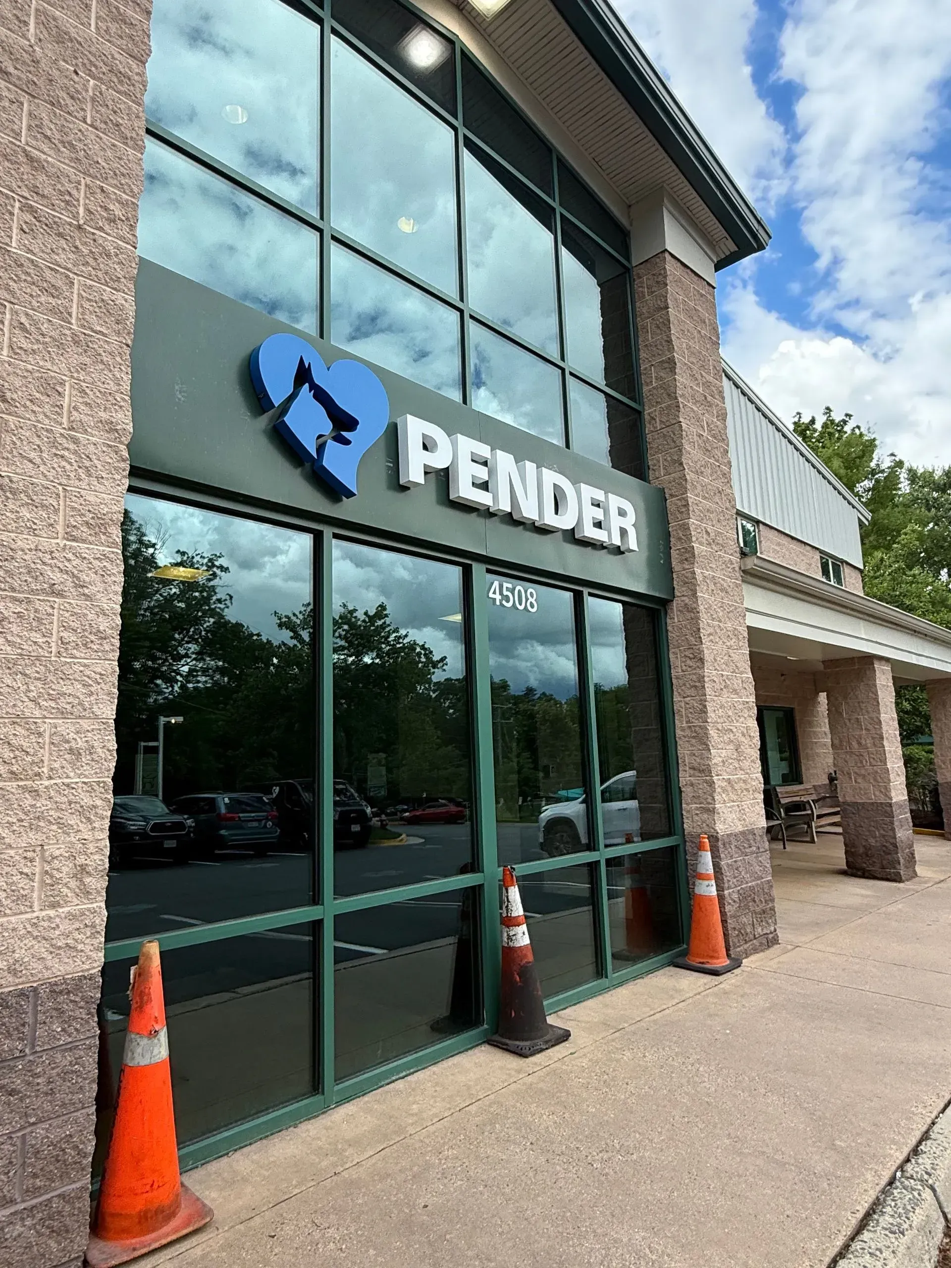 Pender storefront with glass windows, brick columns, and orange traffic cones outside.