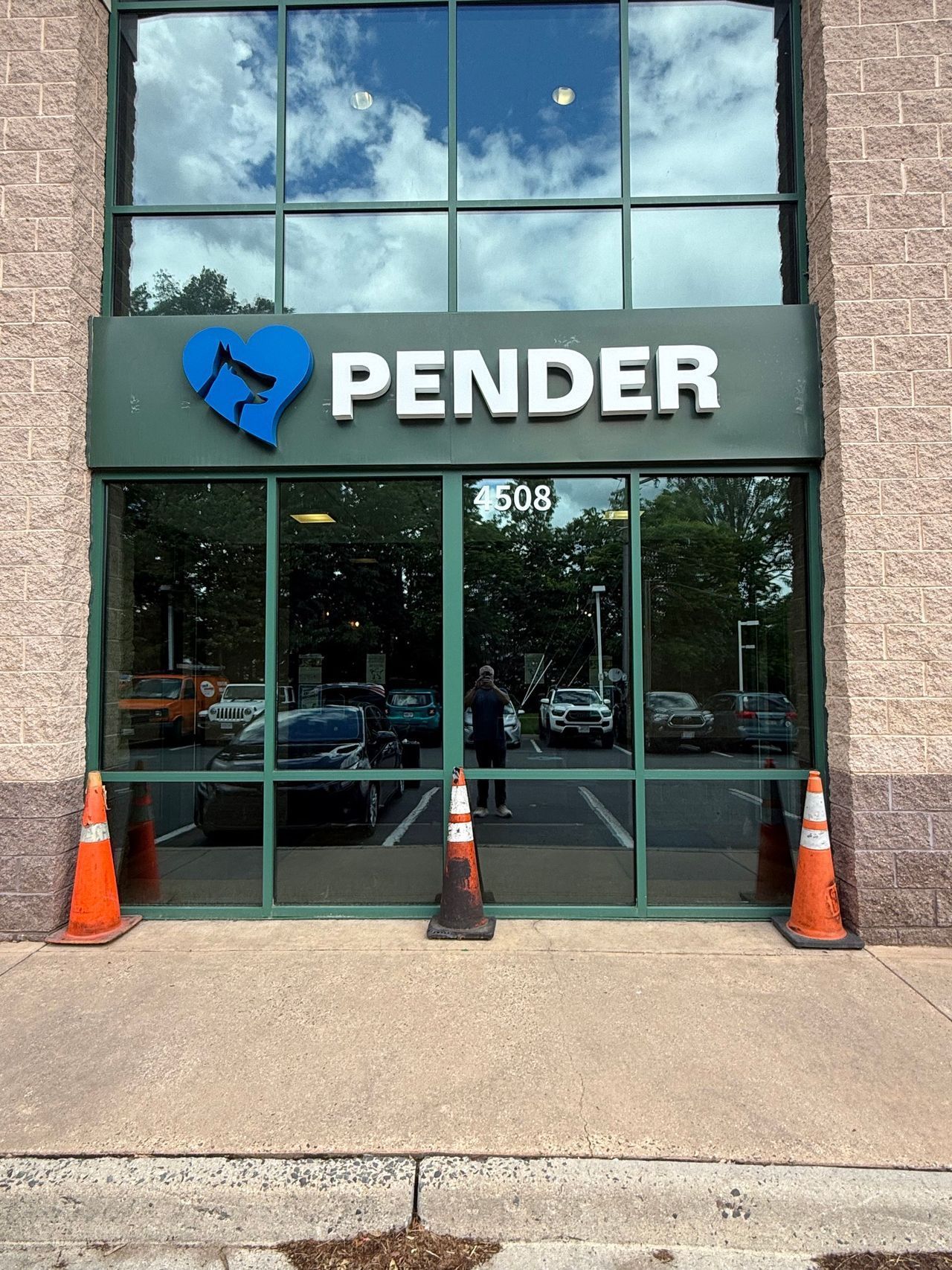 Storefront with Pender sign, blue logo, glass windows, and orange cones outside