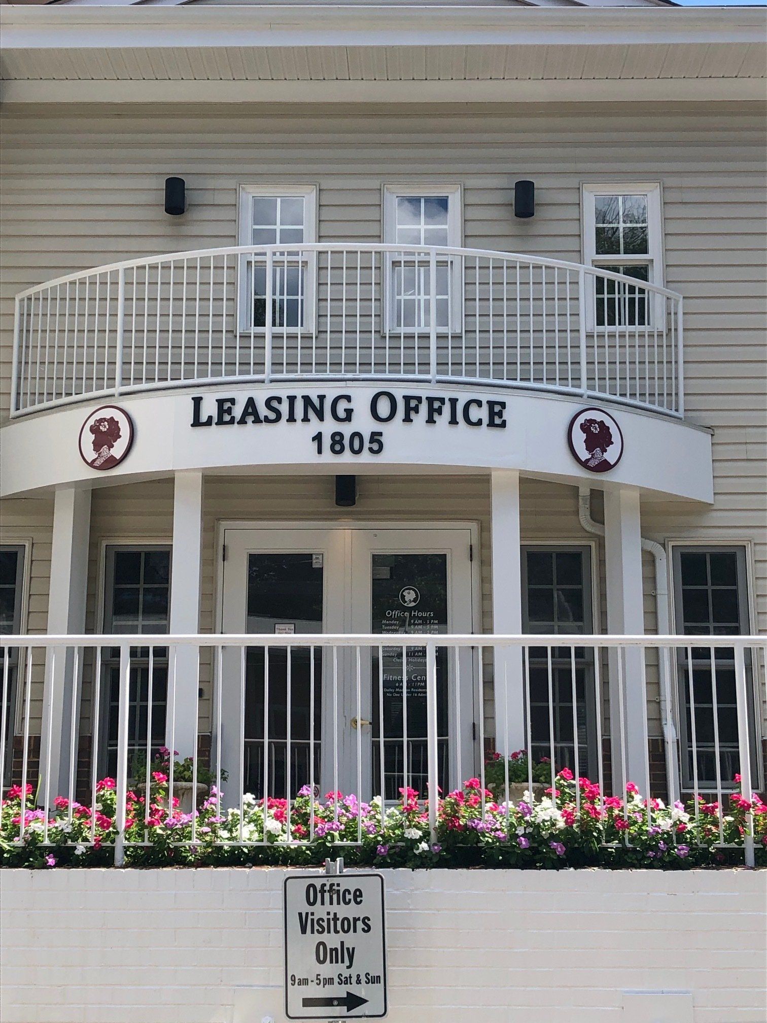 Leasing office building entrance with white balcony, black lanterns, and flower bed