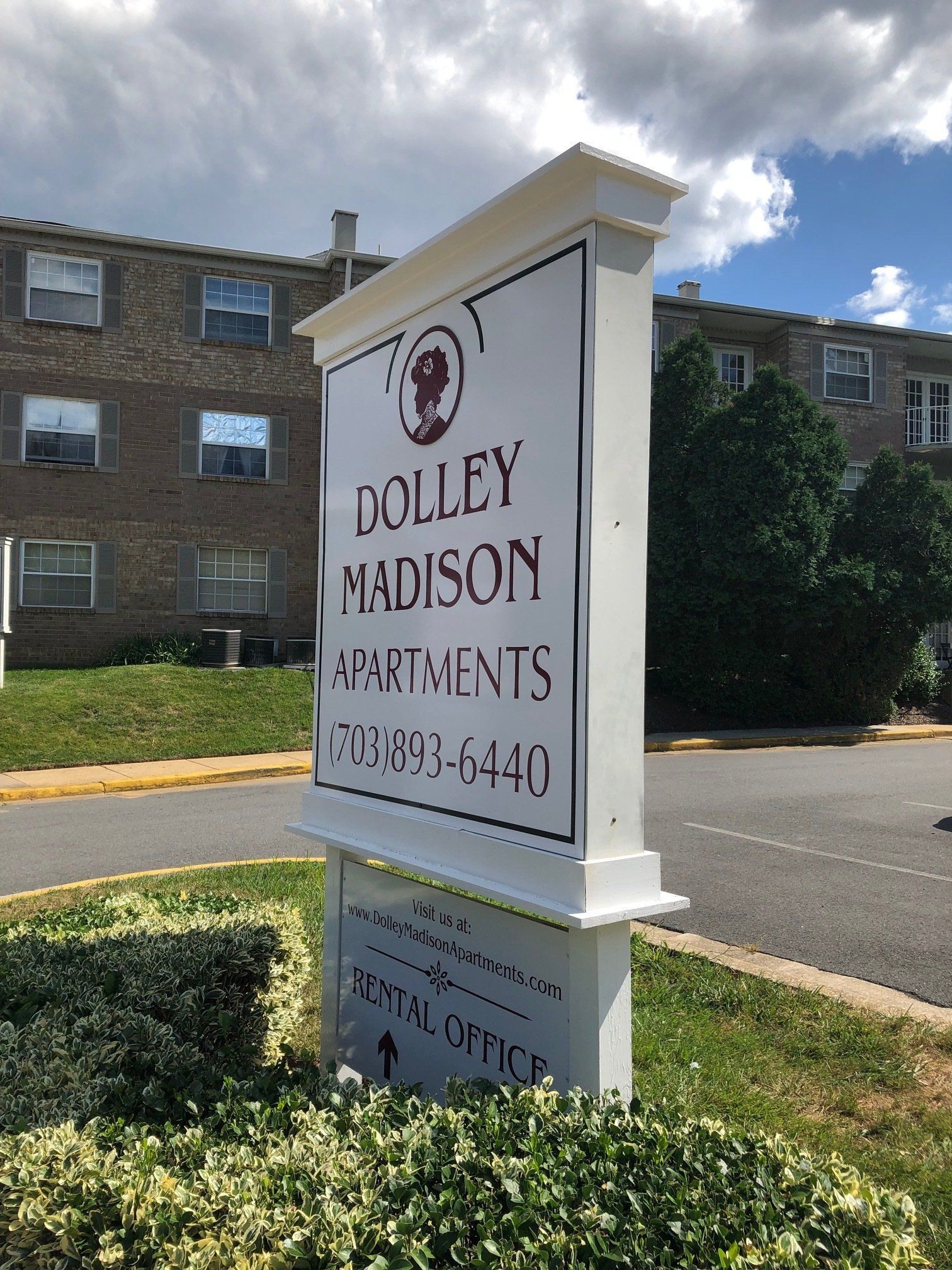 Dolley Madison Apartments sign in front of brick buildings and green landscaping under a blue sky