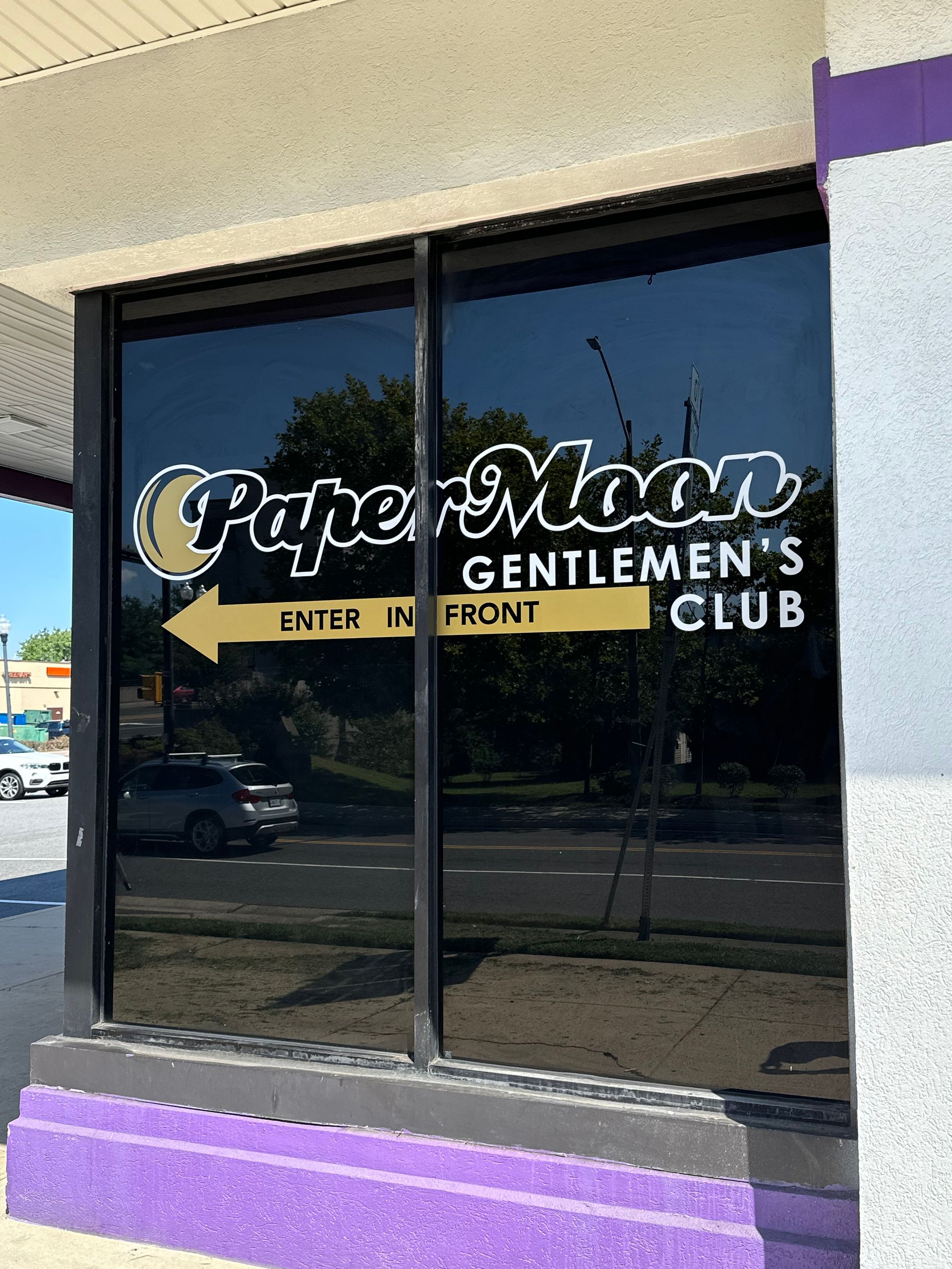 Storefront window with “Paper Moon Gentlemen’s Club” sign and a left-pointing “Enter in Front” arrow