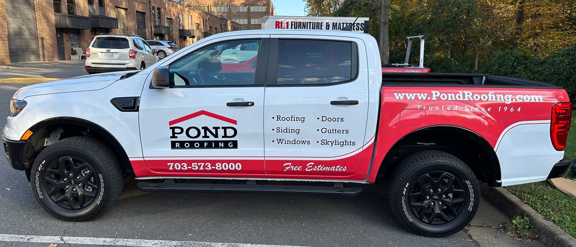 White and red service pickup truck with company logos parked outdoors on a street.