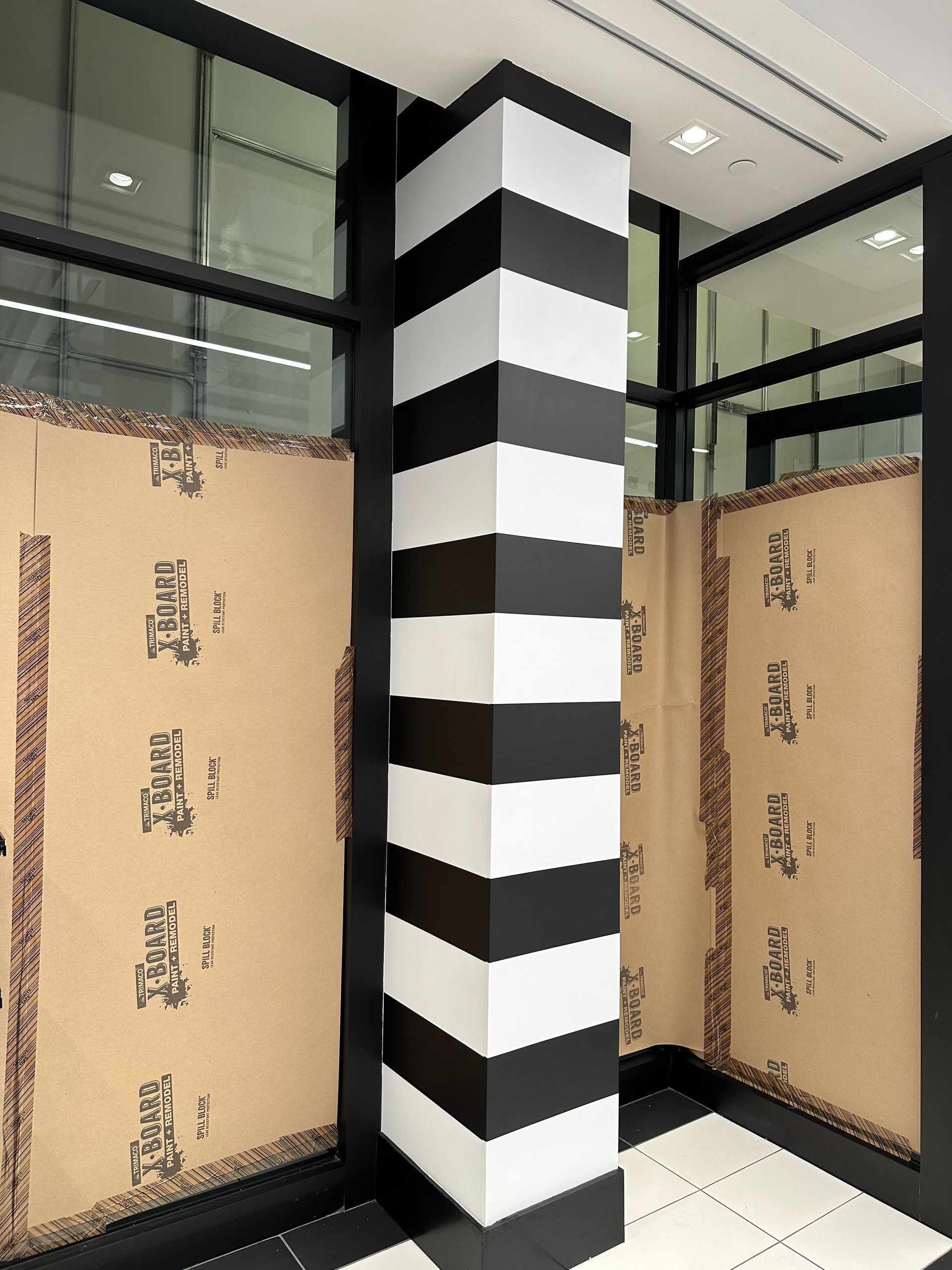 Black-and-white striped column in a modern interior with large windows and tan wall panels